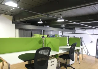 Un espace de coworking moderne chez Nuage B à Montréal, avec des panneaux de séparation verts, des chaises ergonomiques et des bureaux élégants dans un loft industriel.