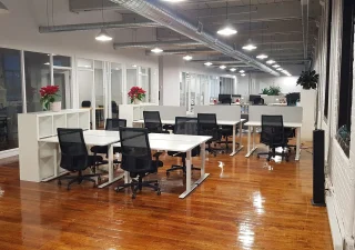 Un espace de coworking spacieux et moderne chez Nuage B à Montréal, avec des postes de travail ouverts, des chaises ergonomiques et une abondante lumière naturelle dans un cadre au design industriel.