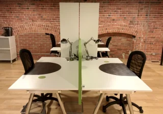 Un espace de coworking élégant chez Nuage B à Montréal, avec des bureaux partagés au design moderne, des chaises ergonomiques et un mur de briques apparentes pour une ambiance industrielle chaleureuse.